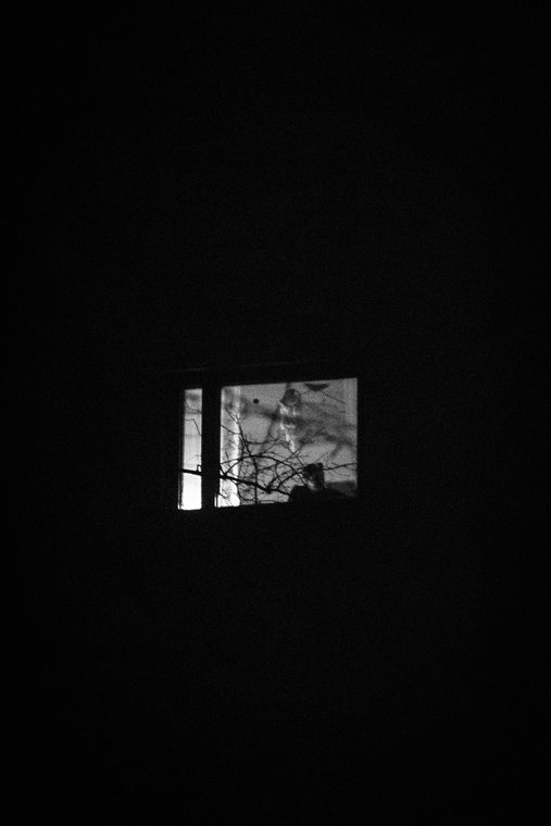 A tiny lit window floats in an otherwise dark wall.