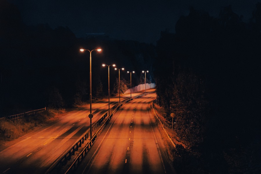 Two empty divided roads curve beneath a sequence of orange streetlights in the night.